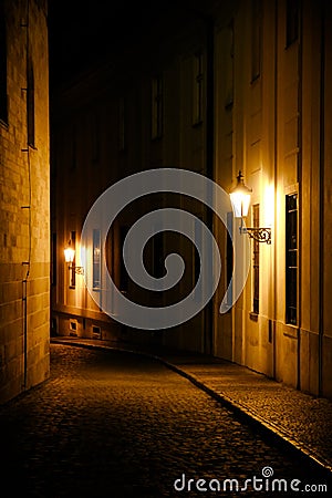 Old lanterns illuminating a dark alleyway medieval street at night in Prague, Czech Republic. Low key photo with brown yellow tone Stock Photo