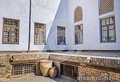 Old lattice windows in the white wall and big clay jugs in inner yard of the ancient Ark of Bukhara, Uzbekistan. Stock Photo