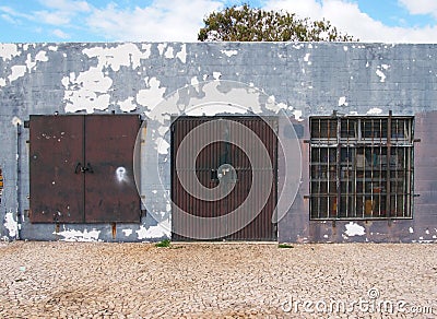 Old low run down grey painted storage building with rusty metal bars and closed metal security shutters padlocks on the door Stock Photo