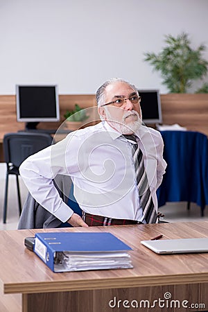 Old male employee suffering from radiculitis at workplace Stock Photo