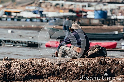 Old man resting on the shore of the bay, watching people pass by and in front of him . Stock Photo