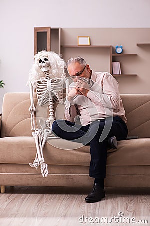 Old man sitting on the sofa with the female skeleton Stock Photo