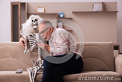 Old man sitting on the sofa with the female skeleton Stock Photo