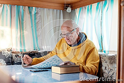 Old man sitting at table in recreational vehicle and solving crossword Stock Photo