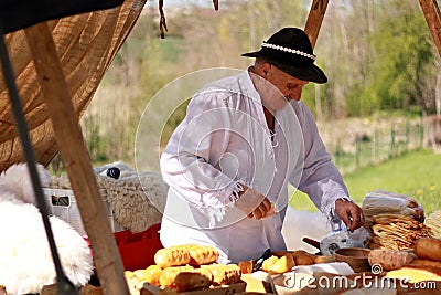 An old man in traditional clothing sells cheeses at a street market. Editorial Stock Photo