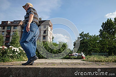 Old man walking near an senior woman sleeping on a bench, in the district of Doni Dorcol, belgrade Editorial Stock Photo