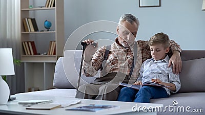 Old man watching photo album with grandson, recalling stories from happy youth Stock Photo