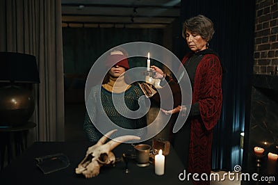 Old mature gypsy fortune teller reading witchcraft spell from book for woman Stock Photo