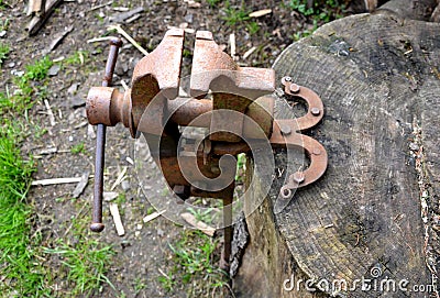 A rusty vice located outside on a stump is used to grip objects for work, also to sharpen a hand scythe. Stock Photo