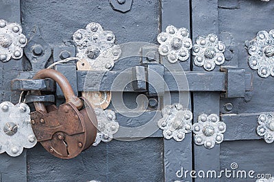 The old metal wrought-iron door is locked with a padlock. Closed metal lock. Stock Photo