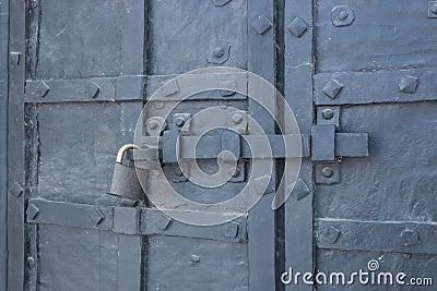 The old metal wrought-iron door is locked with a padlock. Closed metal lock. Stock Photo