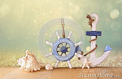 Old nautical wood wheel, anchor and shells on wooden table over abstract glitter background Stock Photo