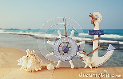 Old nautical wood wheel, anchor and shells on wooden table over sea background. Stock Photo