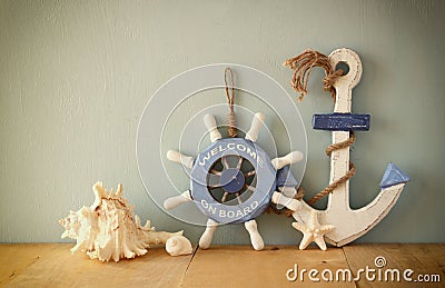 Old nautical wood wheel, anchor and shells on wooden table over wooden background. vintage filtered image Stock Photo