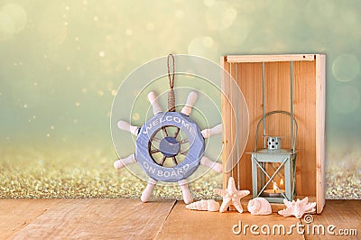 Old nautical wood wheel, lantern and shells on wooden table over wooden glitter background Stock Photo