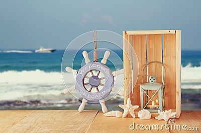 Old nautical wood wheel and shells on wooden table over sea background. Stock Photo