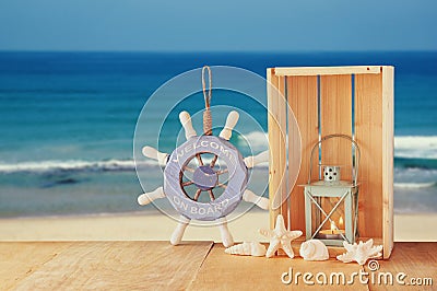 Old nautical wood wheel and shells on wooden table over sea background. Stock Photo