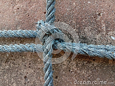 Old nylon ship ropes tied to knot bound around cement electrical post on ground flooring closeup. Stock Photo