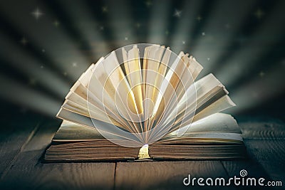 Old open book with falling stars on wooden table, Fairytale book with open pages. Magic light emanating from open old book on tabl Stock Photo
