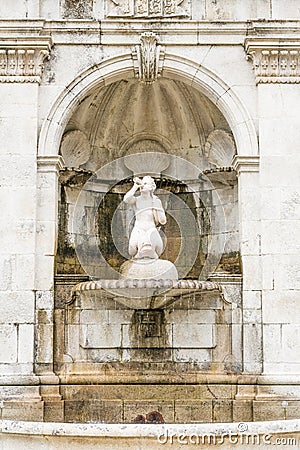 Old ornate water fountain set in a white stone wall with a statue and shell ornamentation Stock Photo