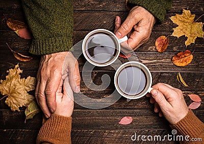 Old people holding hands. Closeup. The senior people hand holding a cup of coffee on wooden rustic table covered with autumn Stock Photo