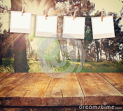 Old polaroid photo frames hanging on a rope with vintage wooden board table in front of abstract forest landscape Stock Photo
