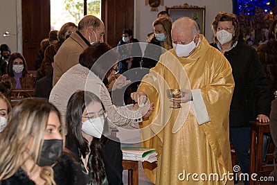 Old priest is distributing communion host to the faithful during a mass in the period of coronavirus. people wearing a protective Editorial Stock Photo