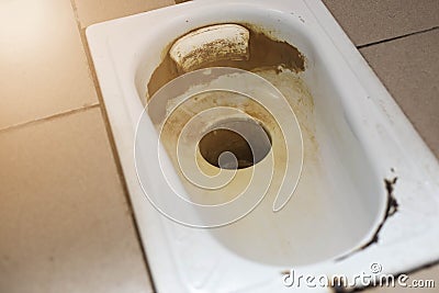An old public floor-standing toilet, with broken tiles and rust. foreground and background blurred with bokeh effect Stock Photo