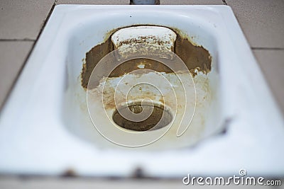 An old public floor-standing toilet, with broken tiles and rust. foreground and background blurred with bokeh effect Stock Photo