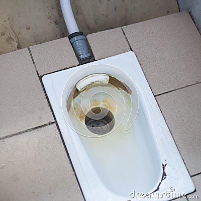 An old public floor-standing toilet, with broken tiles and rust. foreground and background blurred with bokeh effect Stock Photo