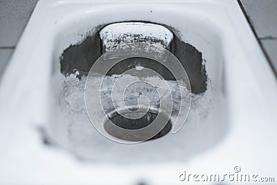 An old public floor-standing toilet, with broken tiles and rust. foreground and background blurred with bokeh effect Stock Photo