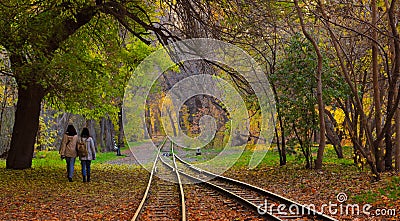 Old Railway in colorful autumn forest: formed by trees and bushes with orange, green leaves, where are two girls walking Editorial Stock Photo