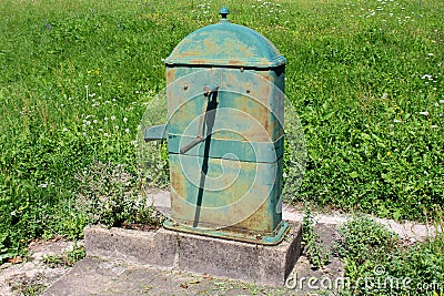 Old rarely used rusted outdoor metal water pump with large rotating handle mounted on concrete stand Stock Photo