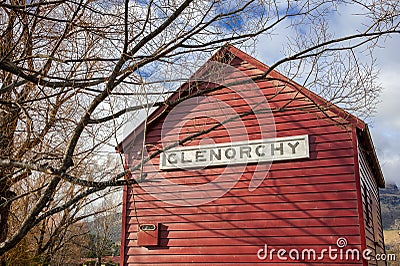 Old red boatshed, Glenorchy, New Zealand. Colourful scene, wooden shed, bare trees and blue, cloudy sky background Stock Photo