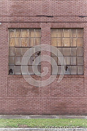 Old red brick building showing signs of abandonment with two busted windows. Stock Photo