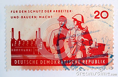An old red east german postage stamp with postal soldiers guarding a factory and a worker Editorial Stock Photo