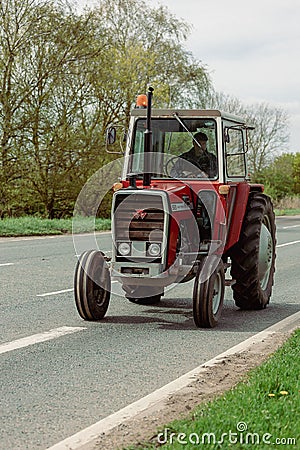 Ely, Cambridgeshire-UK: April 2023: Old red Massey Ferguson 565 tractor being driven on busy main road. Editorial Stock Photo