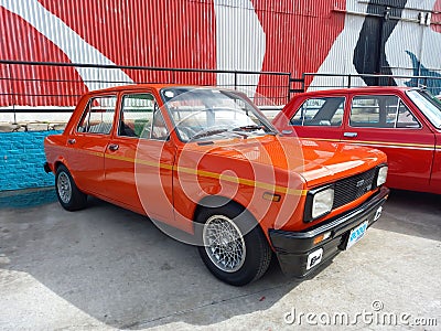 old red 1970s Fiat 128 Europa IAVA sedan in a colorful industrial background. Classic car show Editorial Stock Photo