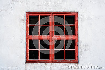 Old red weathered window with squares on white wall with worn texture. Stock Photo