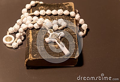 Old religious book with a rosary and white crucifix on top on dark background Stock Photo