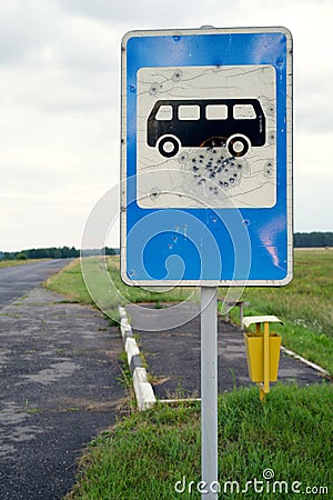 Old road blue bus stop sign damaged by pistole bullets by asphalt road Stock Photo