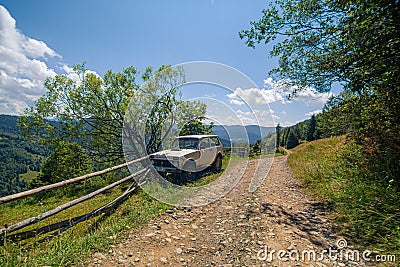 Old russian jeep parked next to wooden fence on the mountain dirty road. Summer day. Mountain tour Editorial Stock Photo