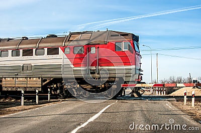 An old russian red train passing across a level crossing, on a small road. Stock Photo