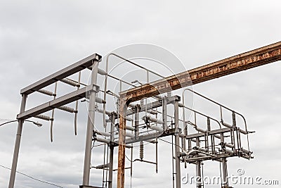 Old rusted overhead gate track beside newer electric power structure, trusses pipe and strain insulators Stock Photo