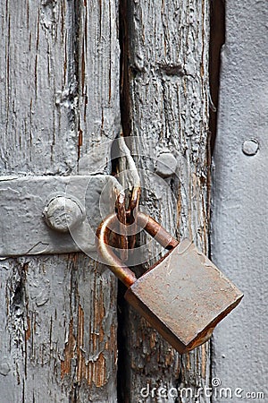 OLD RUSTED PADLOCK ON A WOODEN DOOR WITH FLAKING GREY PAINT Stock Photo