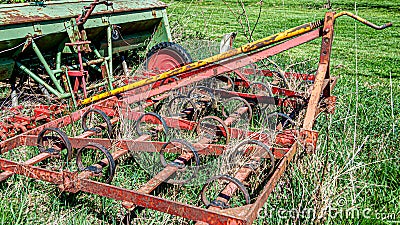 Old, rusty and abandoned red agricultural cultivator next to an old tractor Stock Photo