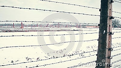 Old rusty barbed wire fence and distant ruined barracks of concentration camp in the snow. 4K steadicam shot Editorial Stock Photo