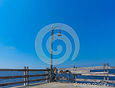 Old Rusty Bicycle Park Under The Damage Lamppost At The Wooden Pier of Marina Beside The Sea Stock Photo