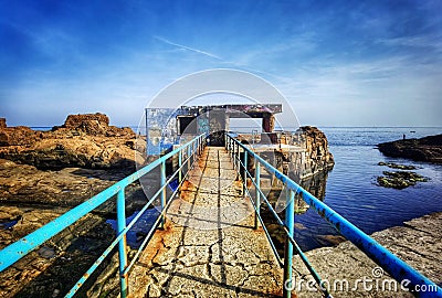 Old rusty bridge leading to the sea water and rocks. Seaside landscape wallpaper Stock Photo