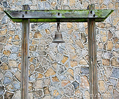 Old Rusty Bronze Metal Bell Hanged on A Green Mossy Wood Pillar In A Stone Pattern Wall Stock Photo